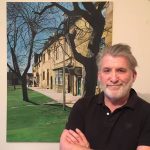Gentleman with a beard standing in front of a painting or a row of Cotswold stone houses