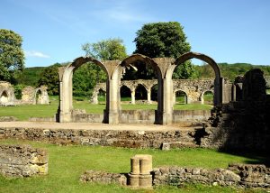 Hailes Abbey ruins are the focal point of the picture, amongst green lawns with trees and blue sky behind.