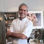 A chef standing in front of a beautifully laid dining table.