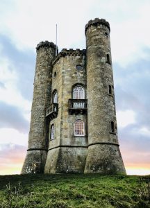 Broadway Tower stands against a sunset on the green hill top