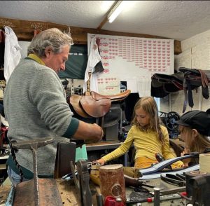 Man working in a saddlery with a young girl watching on