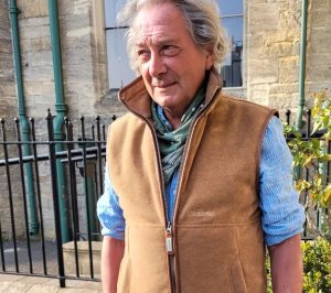 A gentleman in a light brown gillet and blue shirt with the sleeves rolled up.