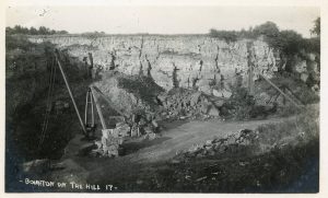 A historic photograph of Bourton on the Hill's now abandoned quarry. The black and white image shows a simple pulley structure with large cut Cotswold stone blocks at its base. The bare rock face is behind,