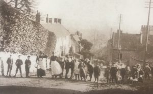 A black and white images of a row of villagers standing across the road, Bourton on the Hill. Taken1895
