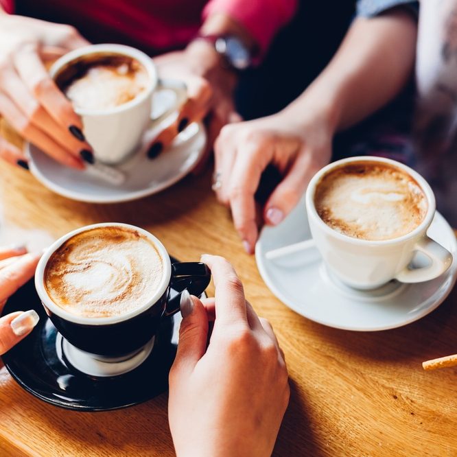 The hands of three people, each holding a coffee cup