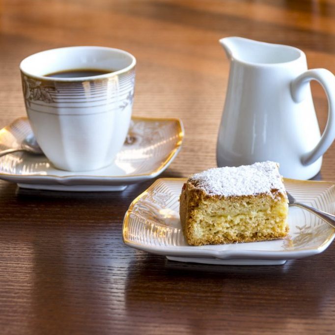 cup of tea on a saucer with a milk jug beside it and a slice of cake on a plate in front